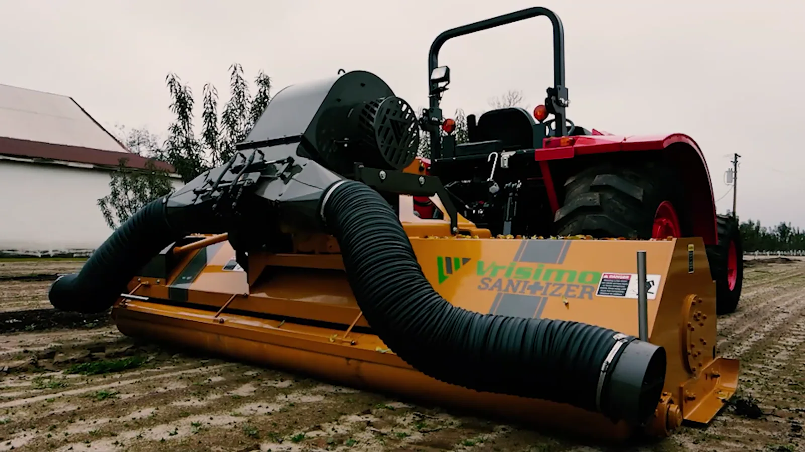 A red tractor with a yellow Vrisimo berm blower attachment and twin black ducts working an orchard floor
