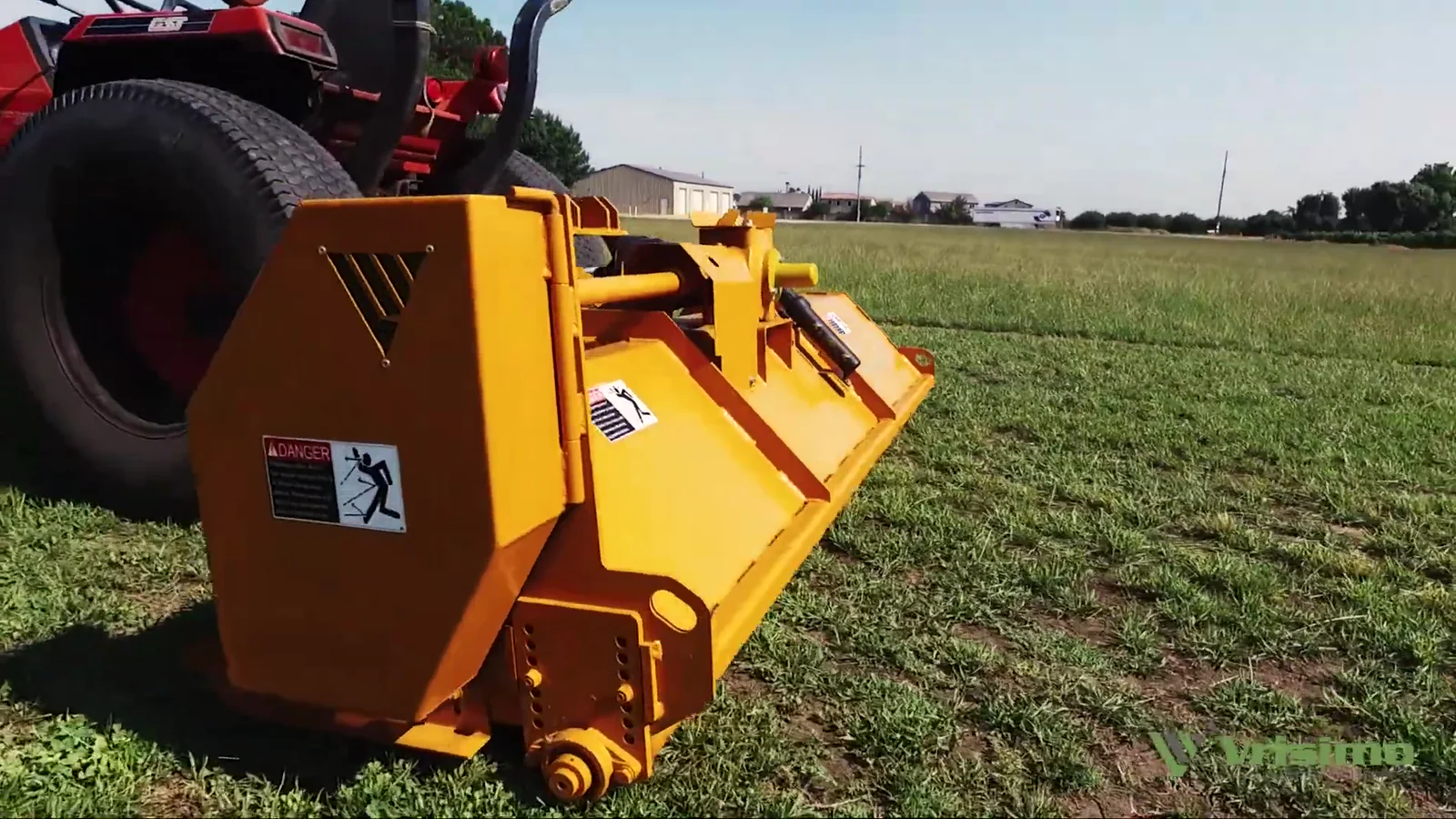 A yellow Vrisimo Super Series flail mower sitting on cut green grass with farm buildings on the horizon