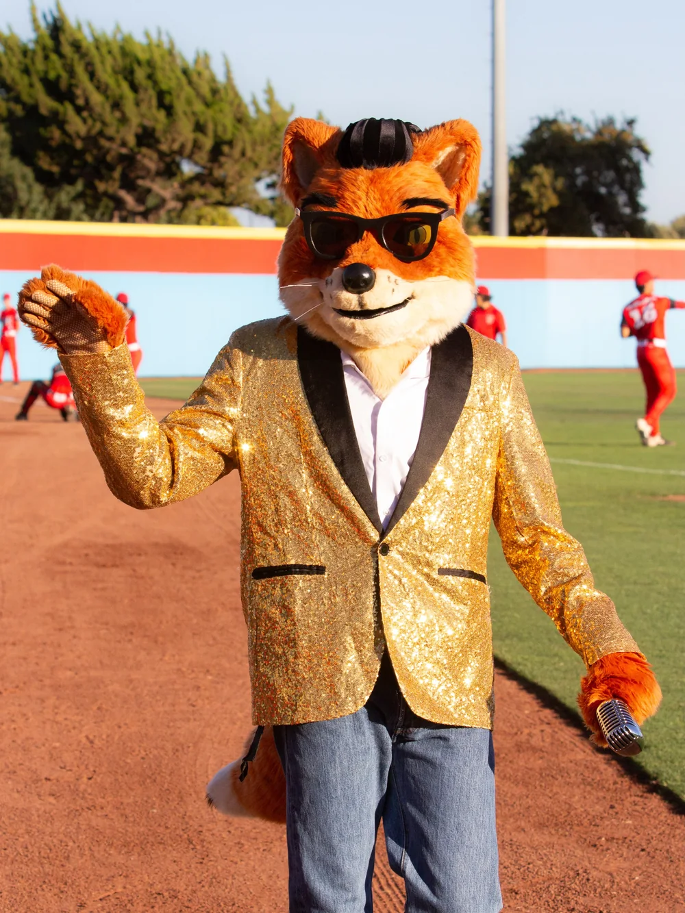 Crooner on the warning track in a gold sequin dinner jacket and sunglasses, holding a vintage microphone, with players warming up behind him