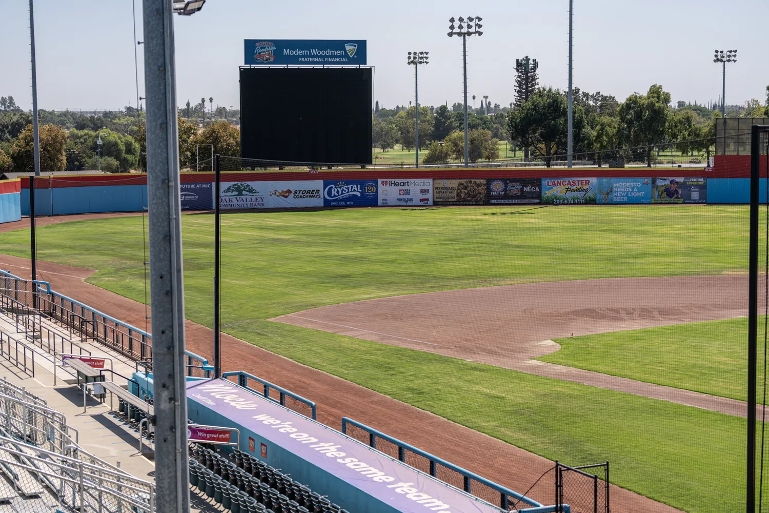 The ballpark from the stands at midday, the scoreboard standing beyond the outfield wall.