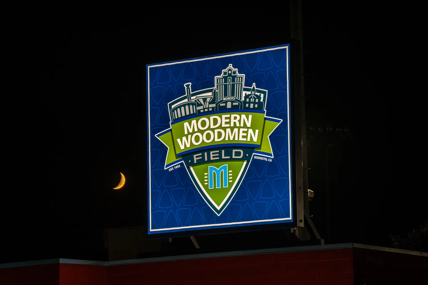 The shield sign lit after dark with a crescent moon above it.