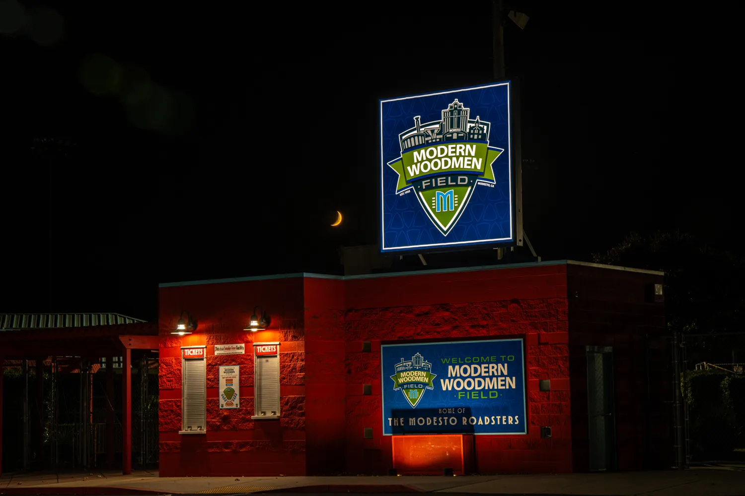 The illuminated sign above the red ticket booth at night.