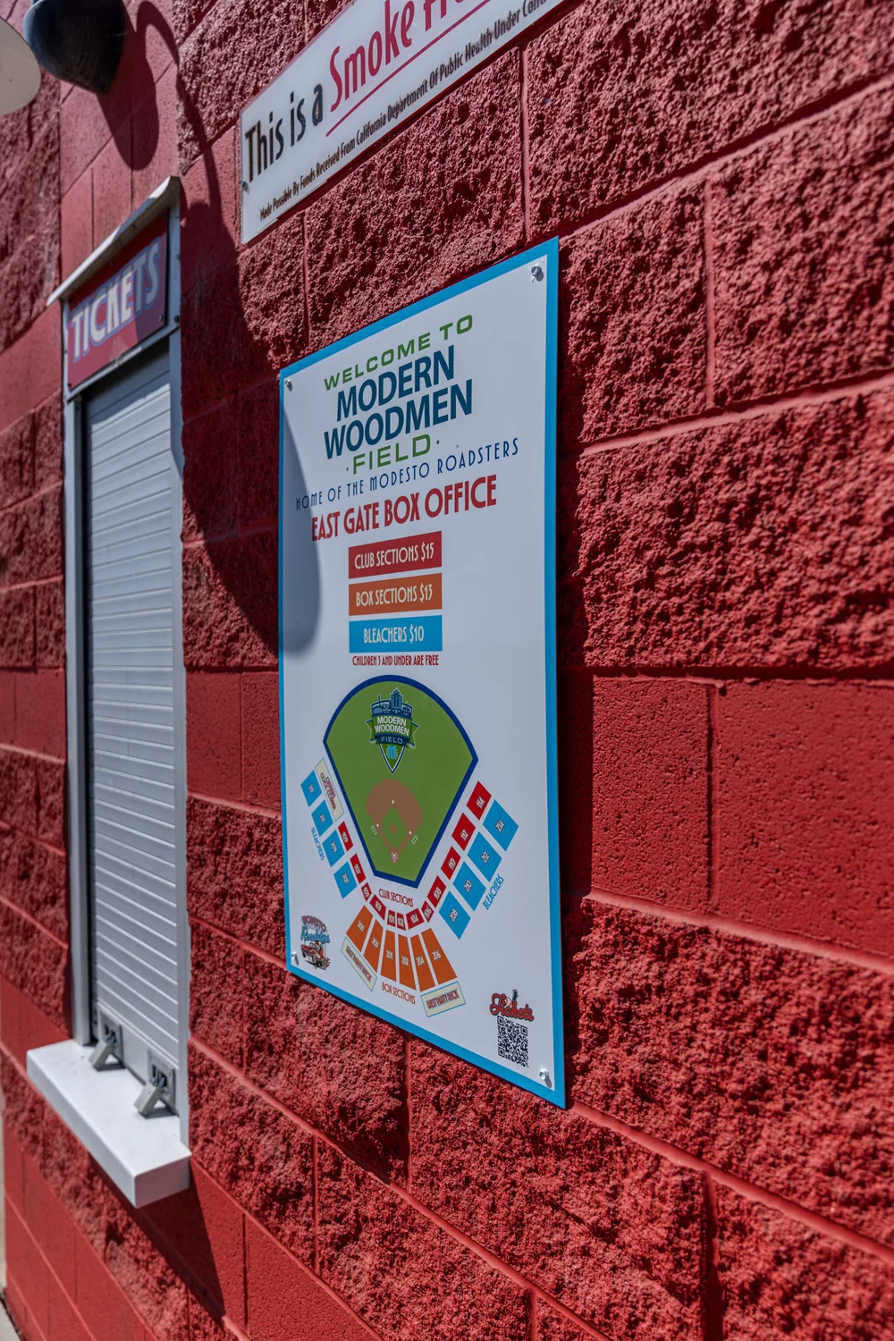 The East Gate box office panel mounted on the red block wall, carrying the Modern Woodmen Field mark above a seating map
