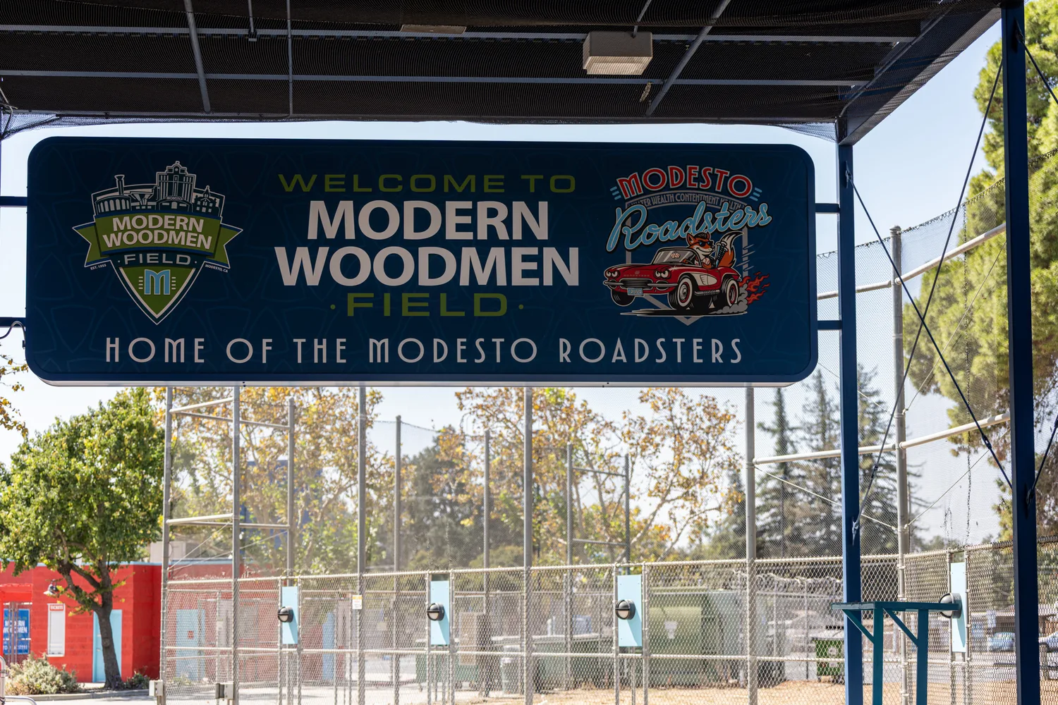 A double-sided illuminated arch sign hanging inside the Party Deck structure, reading Welcome to Modern Woodmen Field, Home of the Modesto Roadsters