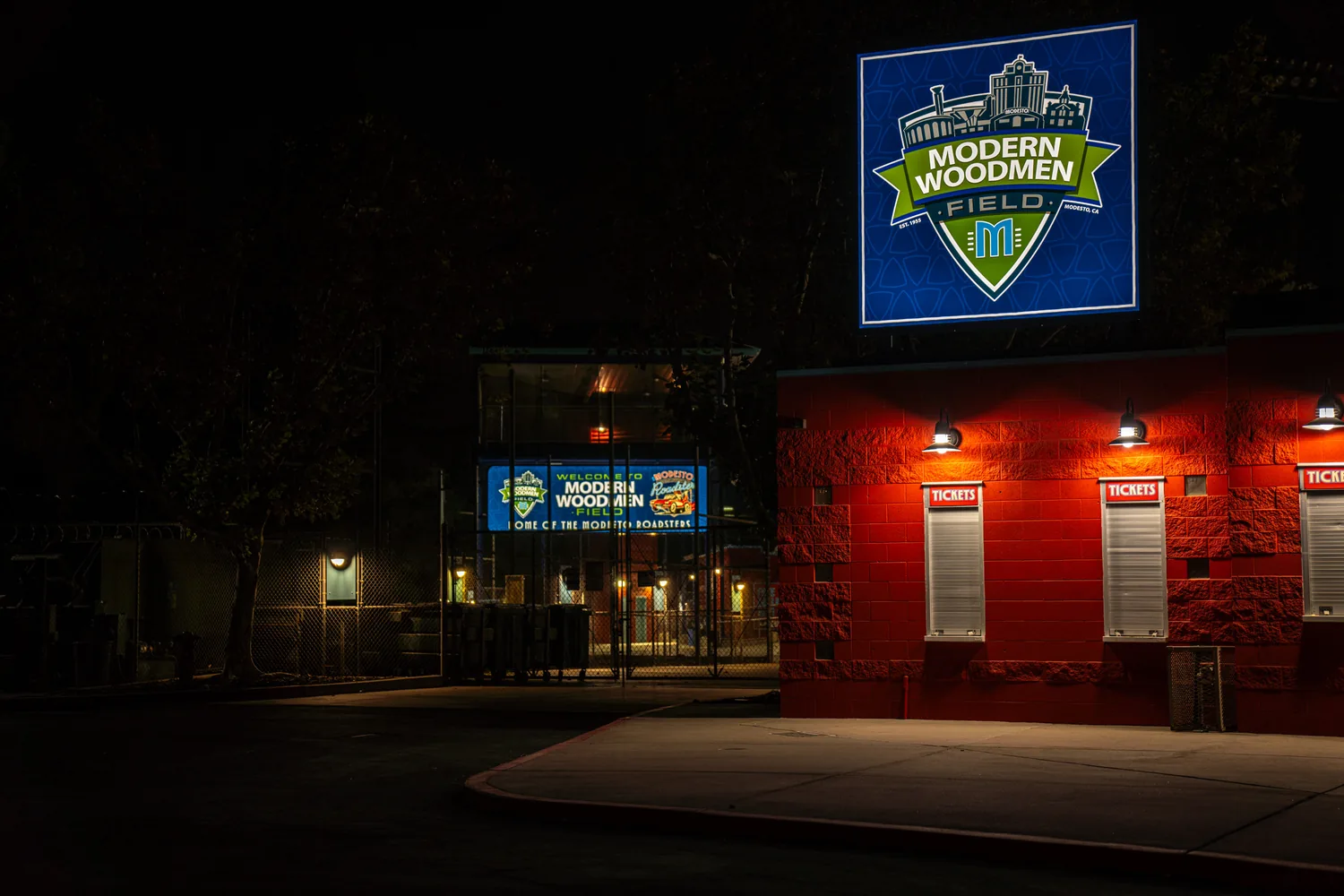 The ballpark entry after dark, the lit sign above the ticket booth the brightest thing on the block