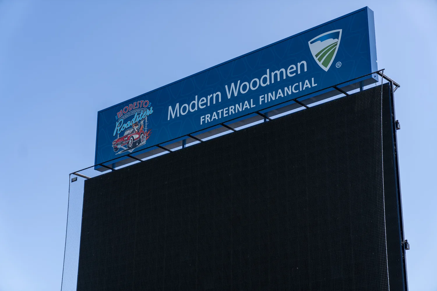 The scoreboard header installed at the ballpark: the Modern Woodmen Fraternal Financial mark on a blue band running the width of the board, the Modesto Roadsters mark at its left end